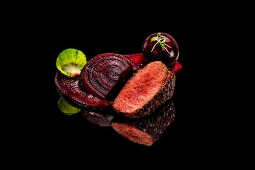 Gros plan d'une tranche de viande, des betteraves et des légumes verts sur une surface noire réflexive.