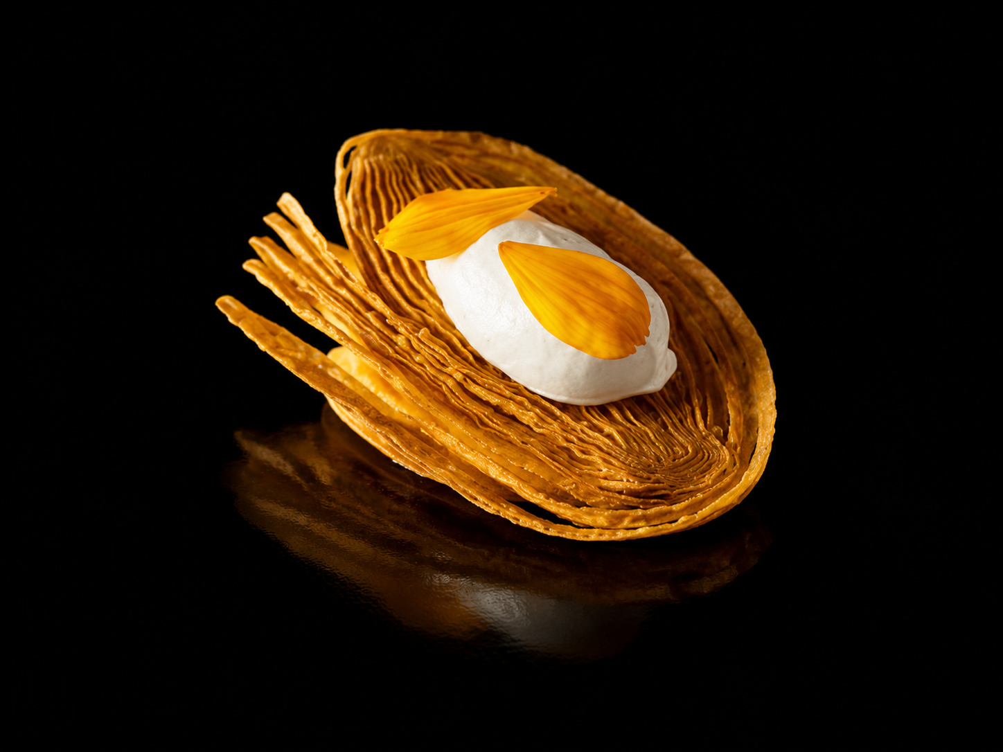 Dessert avec une coque de caramel croustillante, une boule de glace à la vanille et des pétales d'orange