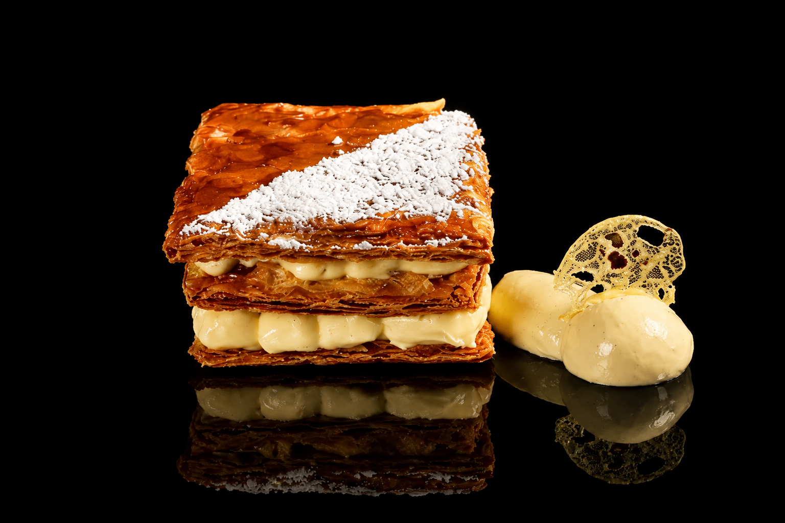 Gâteau feuilleté avec sucre glace, crème pâtissière, et décoration en biscuit de dentelle, présenté avec un biscuit en forme de rouleau et un biscuit en forme de disque.