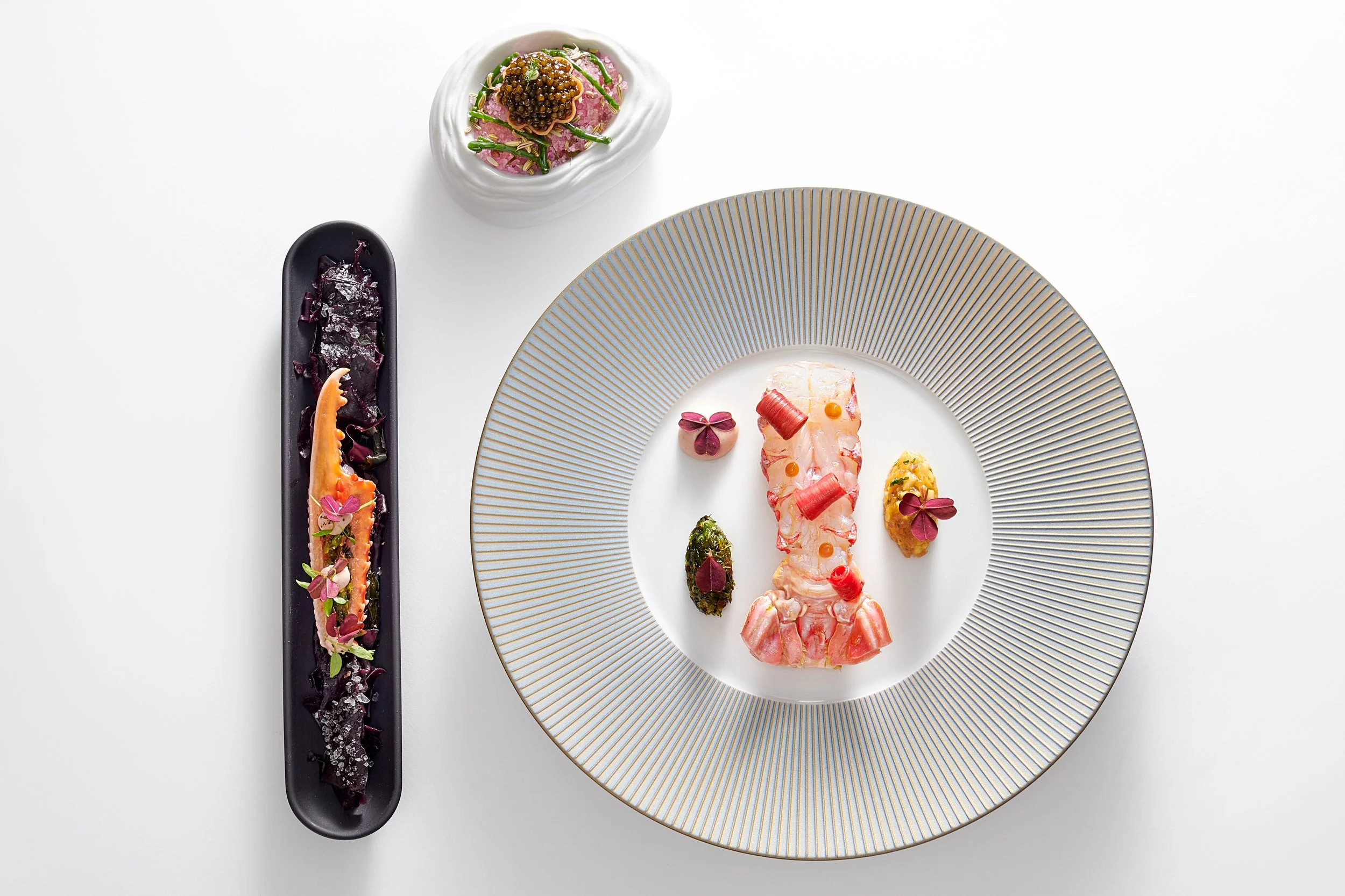 Assiette de cuisine gastronomique avec des plats artistiques, accompagnée d'une autre assiette longiligne avec une préparation colorée, décorée de fleurs comestibles. High-end artistic presentation of food on white background.