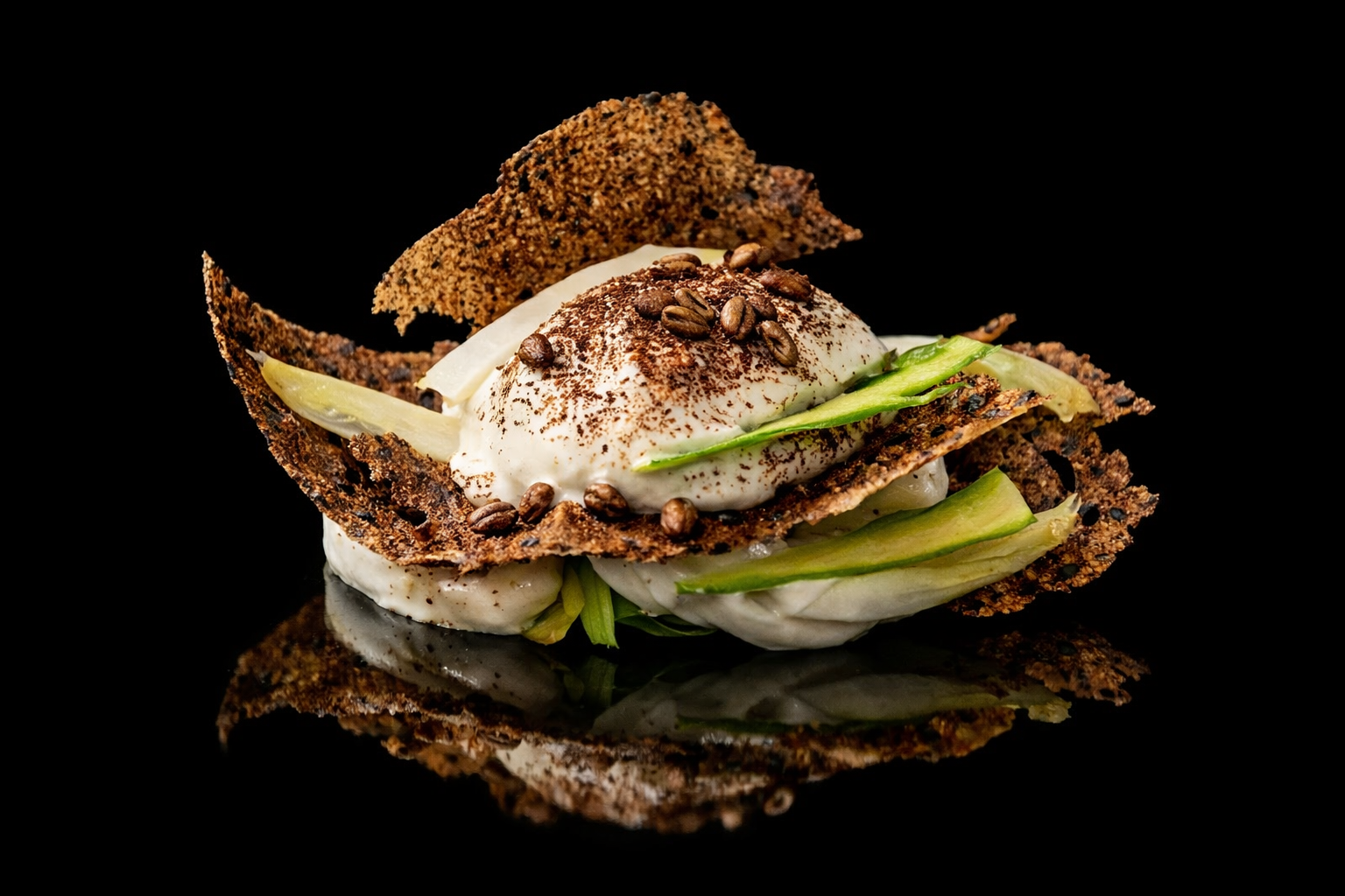 Oeuf au plat à la crème avec des tranches de concombre, entouré de galettes de sarrasin croustillantes, décoré de grains de café, sur fond noir.