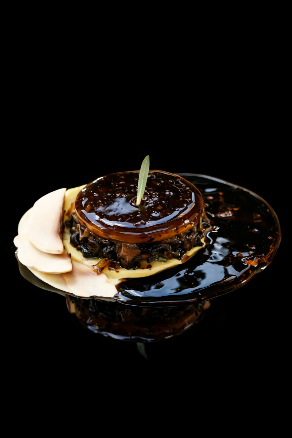 Assiette de tapas avec un gâteau de viande recouvert de sauce, décorée d'une branche de sauge, accompagnée de tranches de champignons en garniture.