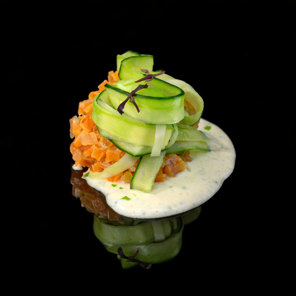 Un plat de tartare de saumon avec des morceaux d'avocat, de concombre en rubans, et une sauce blanche aux herbes, présenté sur un fond noir