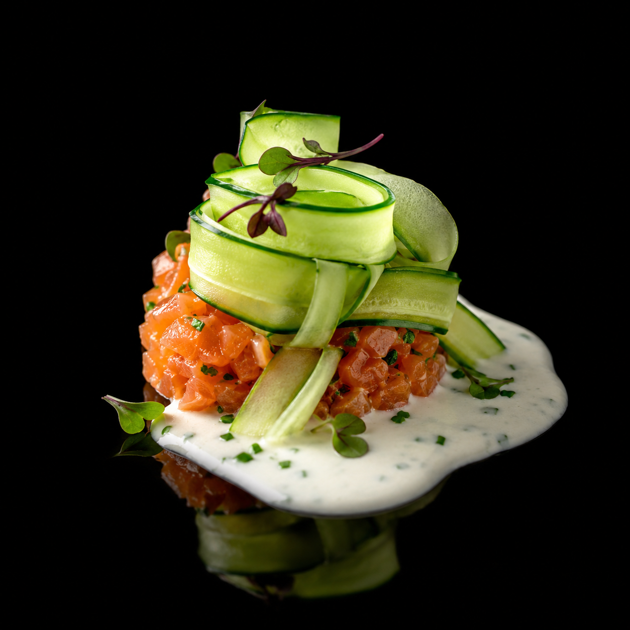 Plate de tartare de saumon avec des rondelles de concombre en ruban, garnie de microgreens, accompagnée d'une sauce blanche