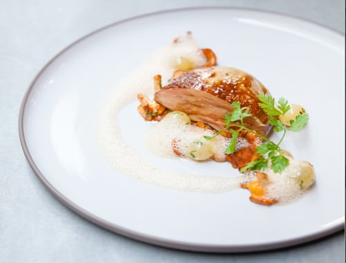 Assiette blanche avec morceau de viande, légumes, et garnish de herbes