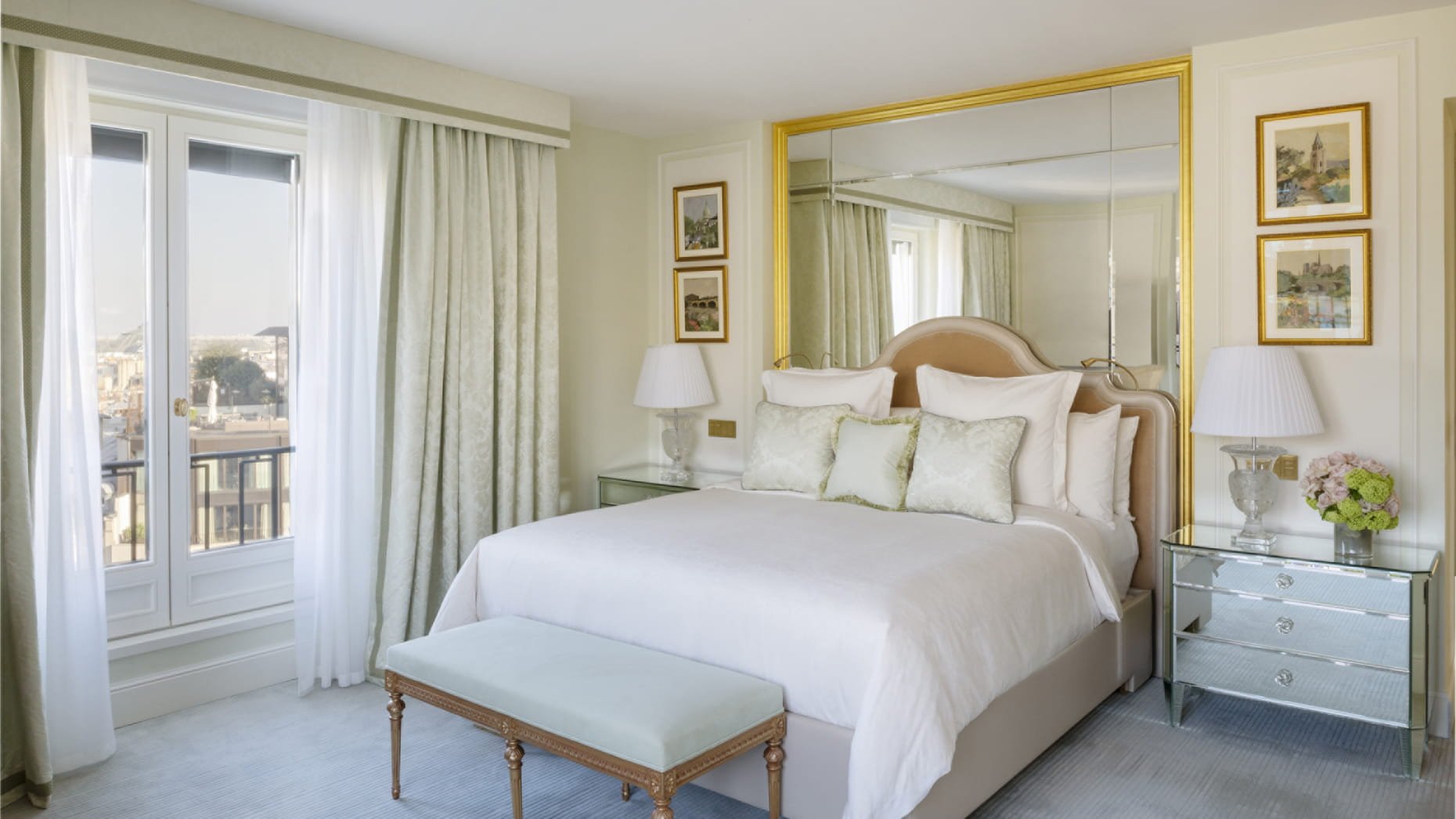 Chambre lumineuse avec grand lit, miroir, lampes et décorations florales.