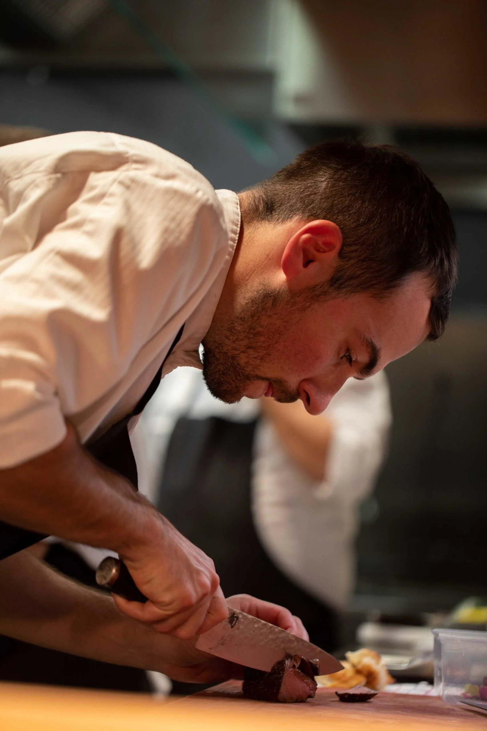 Un homme cuisinier en uniforme blanc coupe de la viande avec un couteau en cuisine.