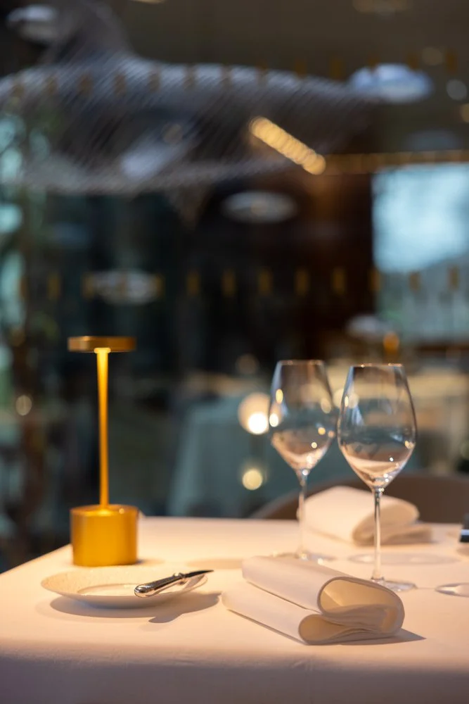 Table de restaurant élégante avec deux verres à vin, un porte-carte blanc, une petite lampe jaune et une nappe blanche, ambiance chaleureuse