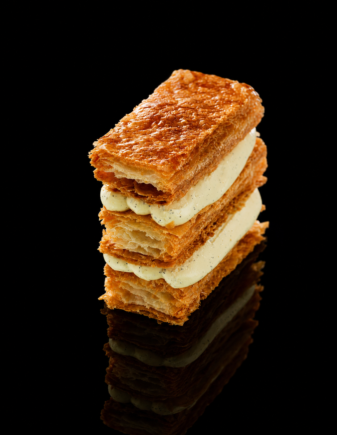 Une pâtisserie composée de plusieurs couches de pâte feuilletée dorée et une crème légère en alternance, présentée sur un fond noir