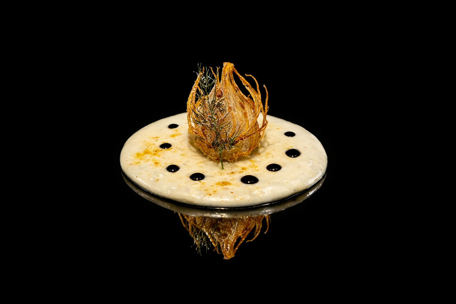 Assiette de nourriture avec un disque blanc, un objet frit ornemental au centre, garnie de petites taches de sauce noire et jaune, sur fond noir.