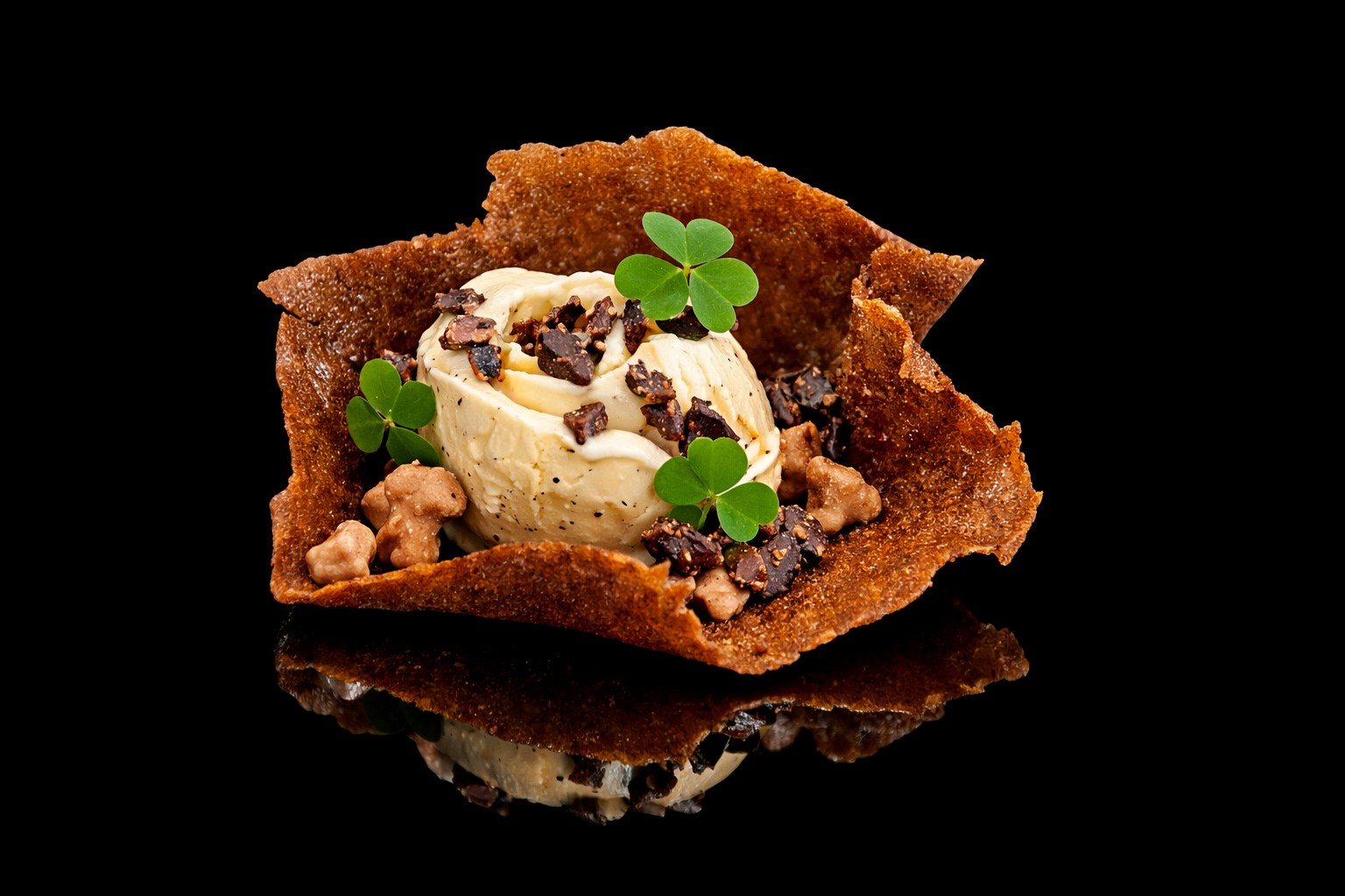 Glace à la vanille garnie de chocolat concassé, entourée d'une feuille de trèfle et de petites choux, servie dans une coupe croustillante en forme de tasse, sur un fond noir.