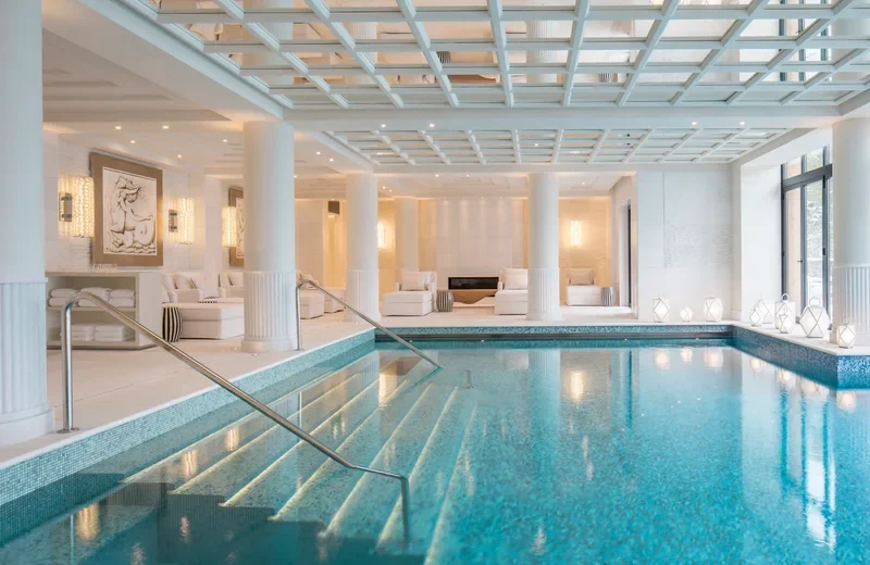 Piscine intérieure dans un spa ou hôtel luxueux, avec des canapés blancs et des lampes décoratives.