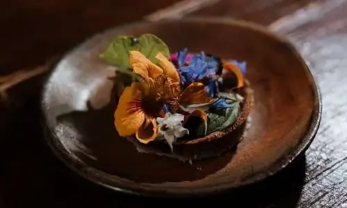 Une assiette en bois avec des fleurs comestibles colorées disposées dessus.