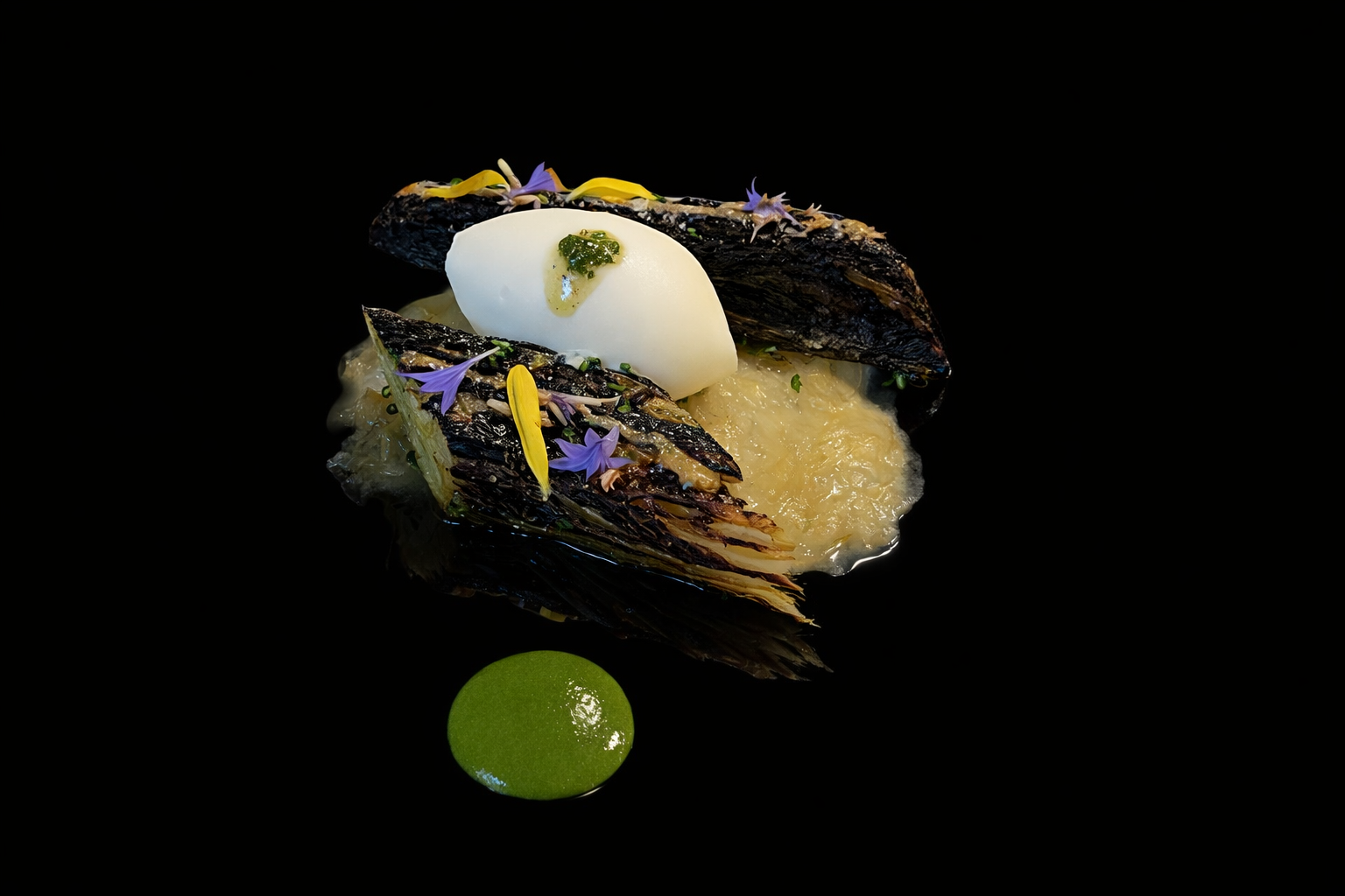 Assiette gastronomique avec des éléments grillés, une quenelle blanche, des fleurs comestibles violettes et jaunes, et une sauce verte, présentée sur un fond noir.