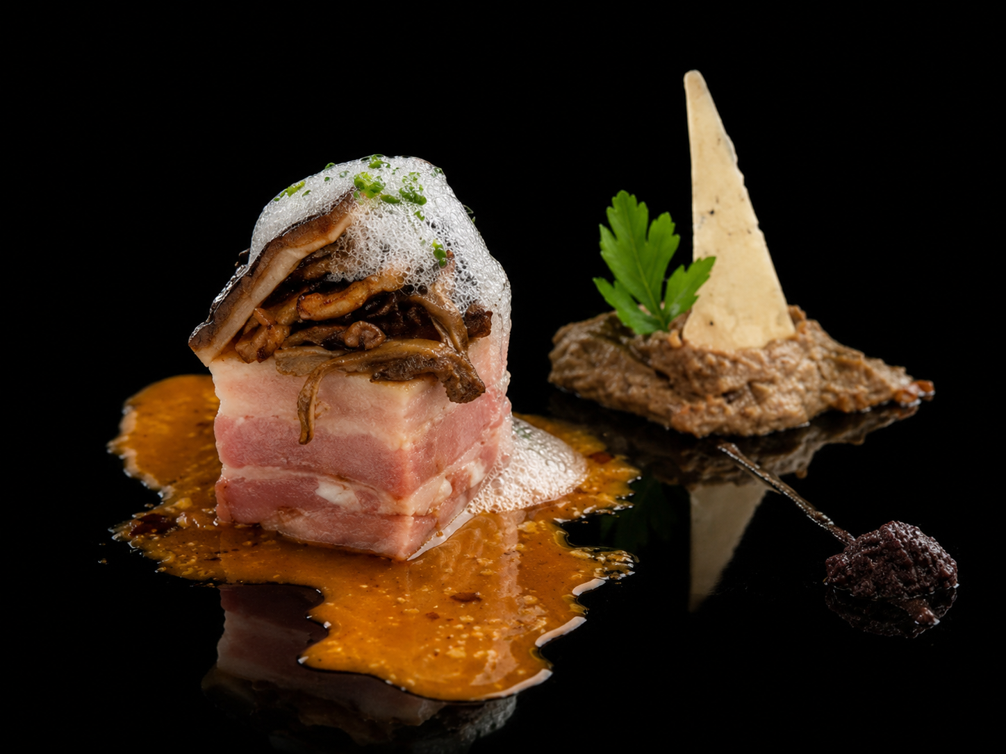 Gourmet plat avec un morceau de viande enroulé de bacon, garni de champignons et d'une mousse, avec une sauce brun-orange, accompagné d'une base de pâté en mousse, décoré d'une feuille de persil, d'une tranche de fromage et d'une petite boule de compote ou de confiture noire, sur fond noir.