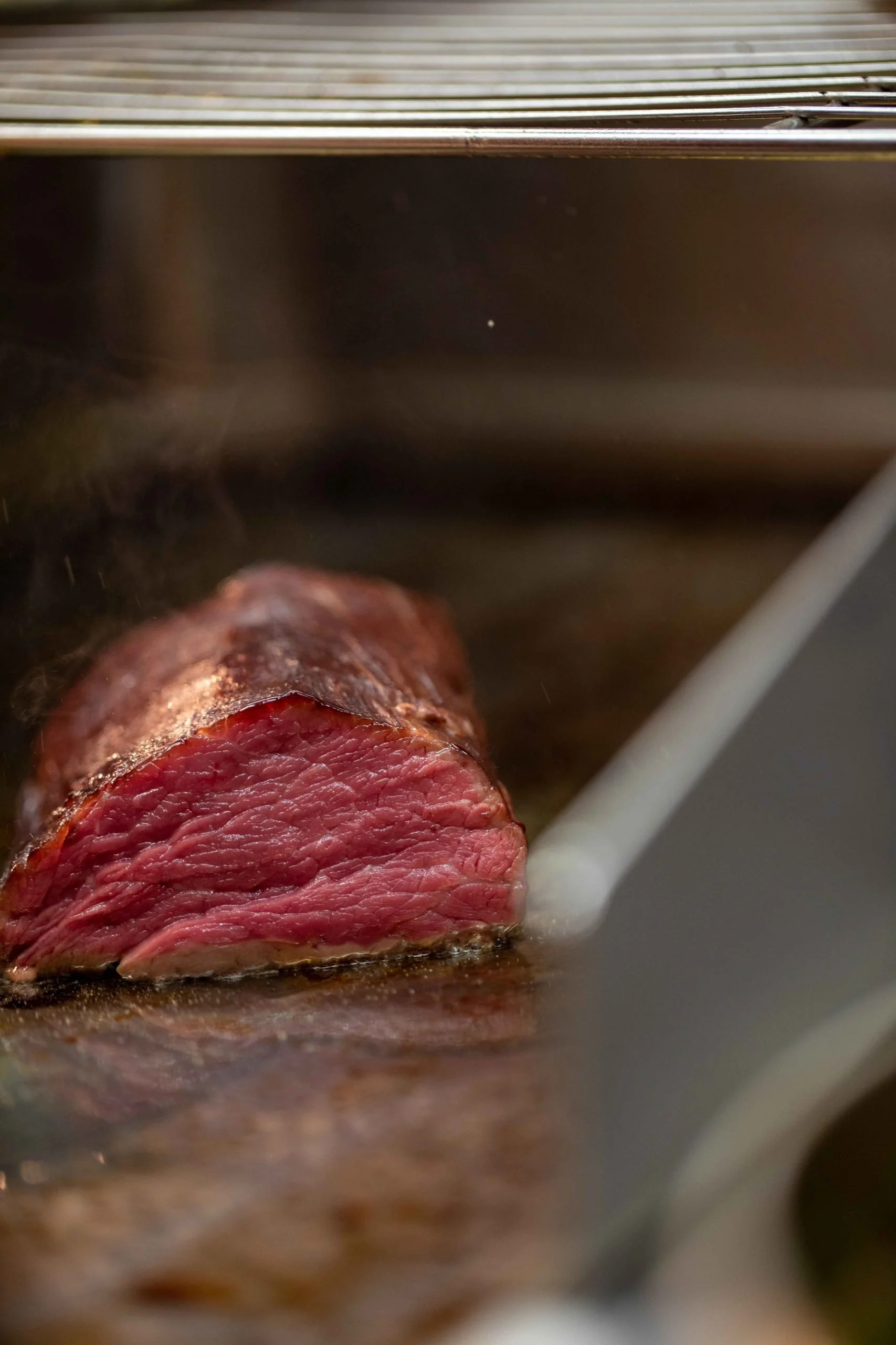 Gros plan sur un morceau de rosbif cuit à point, avec une croûte dorée, reposant sur une surface en fer ou acier inoxydable.