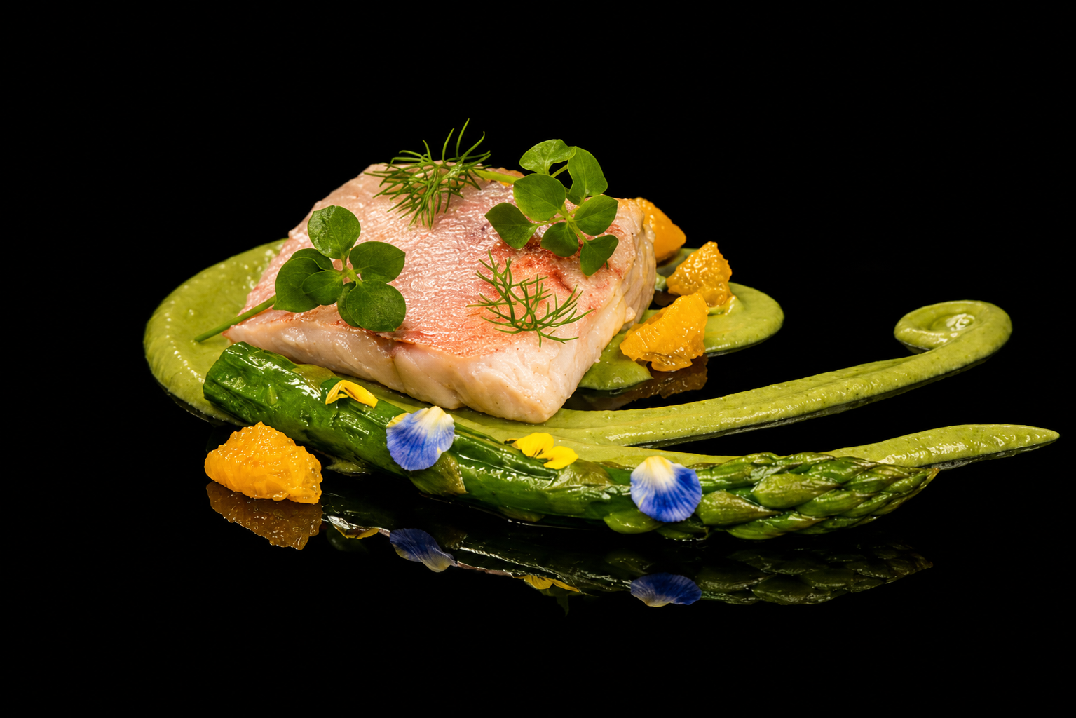 Filet de poisson garni d'herbes et d'agrumes, décoré de asperges, de fleurs comestibles et de purée de légumes verts, présenté sur une assiette noire.