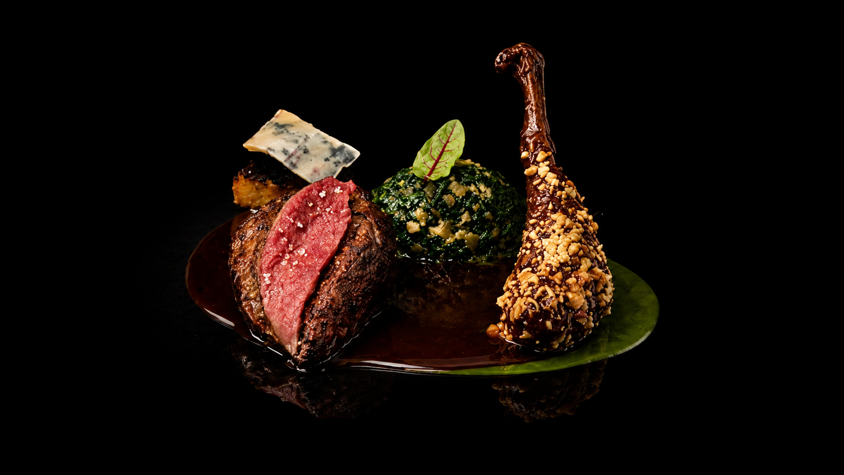 Assiette de viande rouge cuite à point, accompagnée d'une boule de purée verte, d'une sauce sombre, un morceau de fromage bleu et une quenelle enrobée de chocolat et de noisettes hachées.