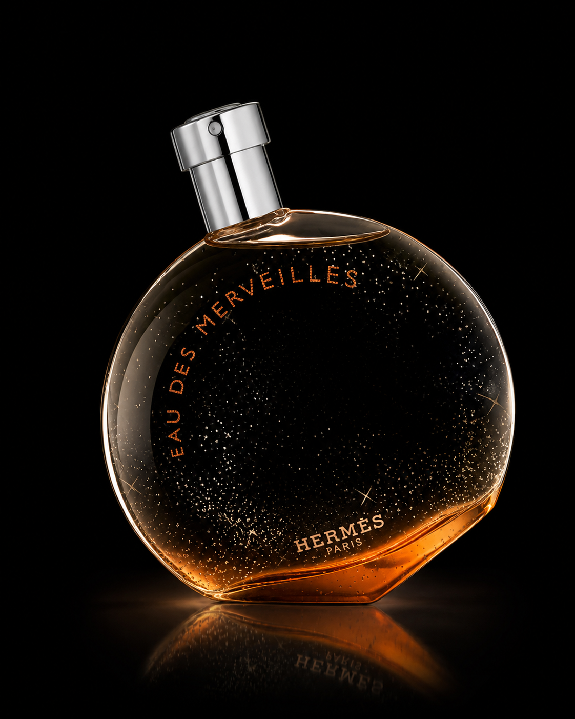 Parfum Hermès 'Eau des Merveilles' dans un flacon rond transparent avec éclats dorés, sur fond noir.