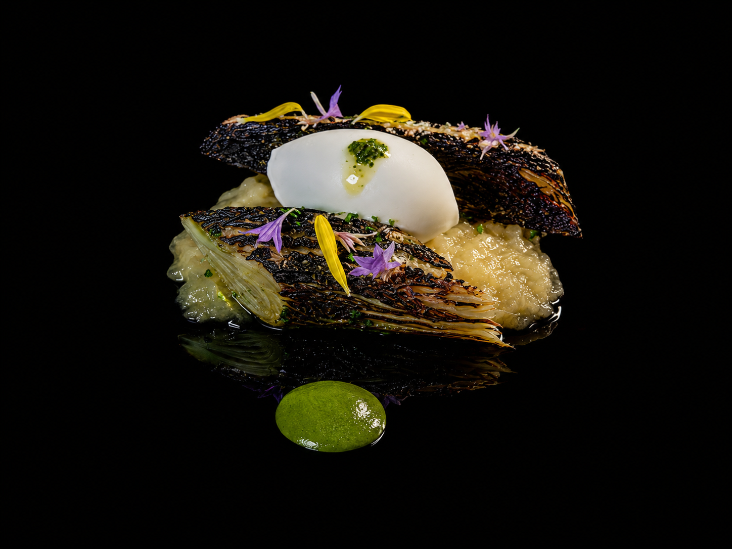 Assiette de poisson grillé avec purée, garniture de fleurs comestibles, œuf mollet et sauce verte, presentation élégante sur fond noir.