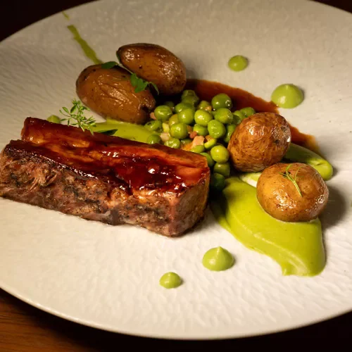 Assiette de viande avec pommes de terre, petits pois, et légumes verts en sauce.