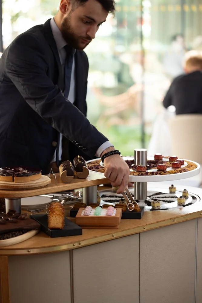 Un homme en costume sert des desserts sur une table lors d'un buffet de pâtisseries