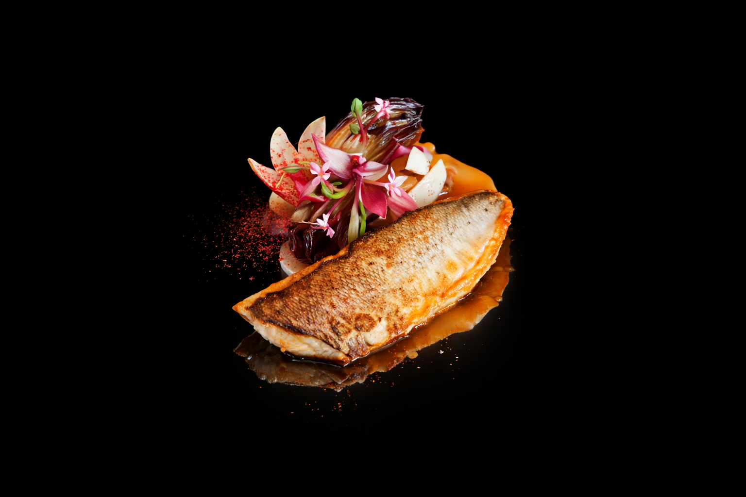 Poisson grillé avec garniture de légumes, fleurs comestibles et sauce sur un fond noir.