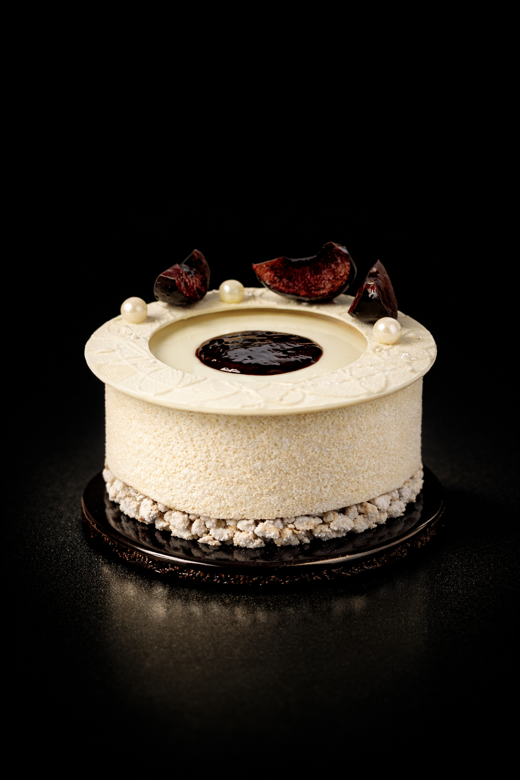 Un gâteau blanc décoré avec des morceaux de chocolat, des perles blanches et une sauce chocolat au centre, présenté sur un fond noir.