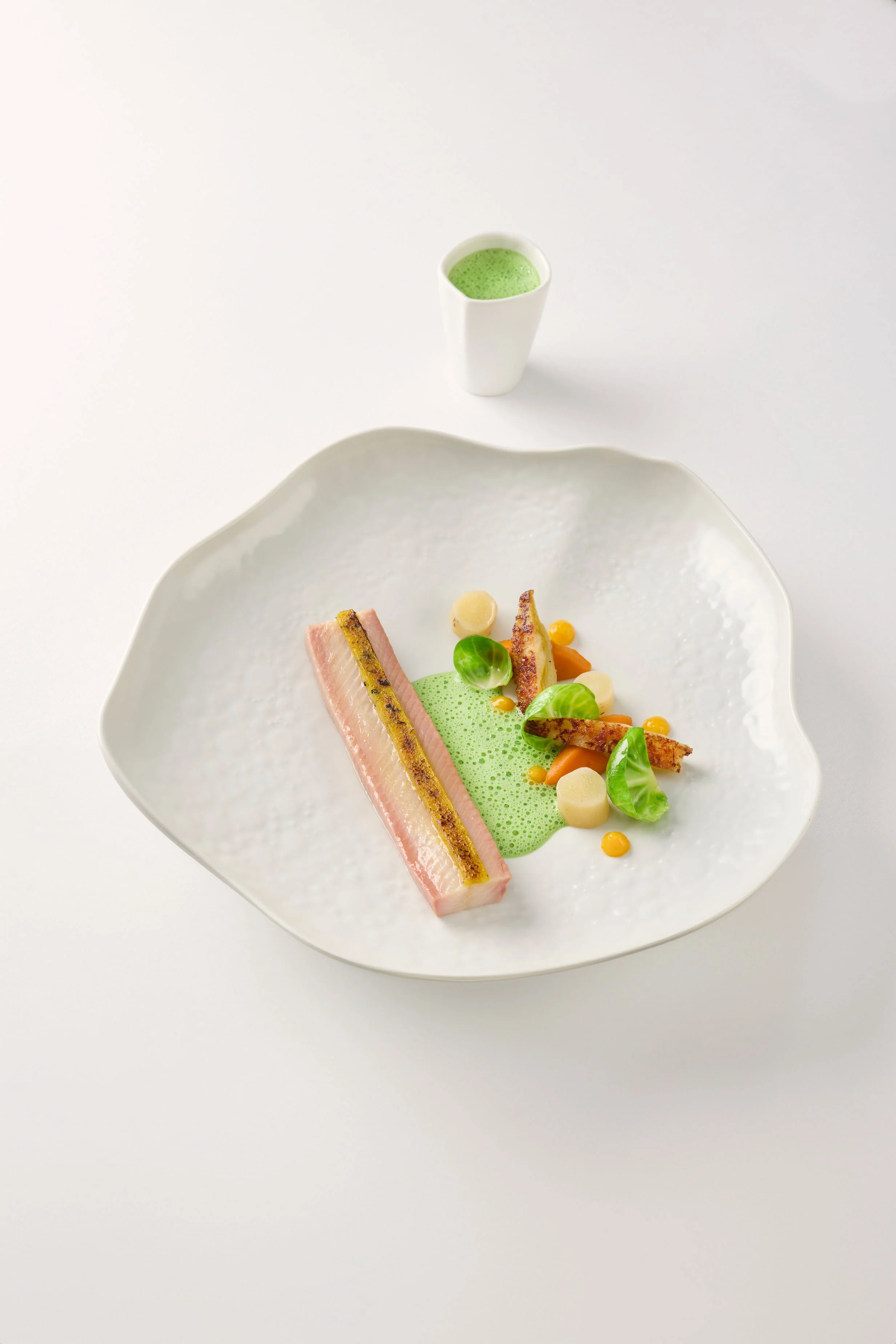Assiette de chef avec poisson, légumes et sauce verte, accompagnée d'un verre de boisson verte.