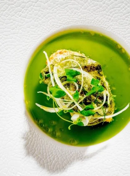 Assiette de soupe verte garnie de légumes verts et herbes, présentée sur une assiette blanche texturée.