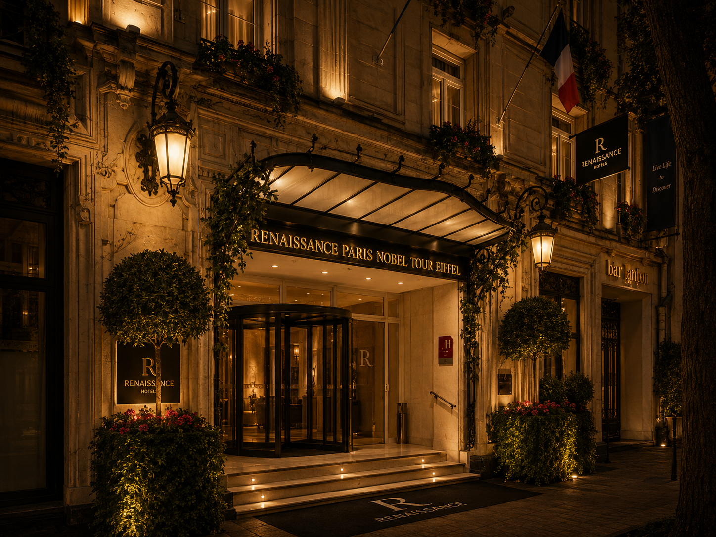 Entrée de l'hôtel Renaissance Paris Nobel Tour Eiffel éclairée la nuit, avec des lanternes, des plantes ornementales et le nom en lettres lumineuses au-dessus de l'entrée.
