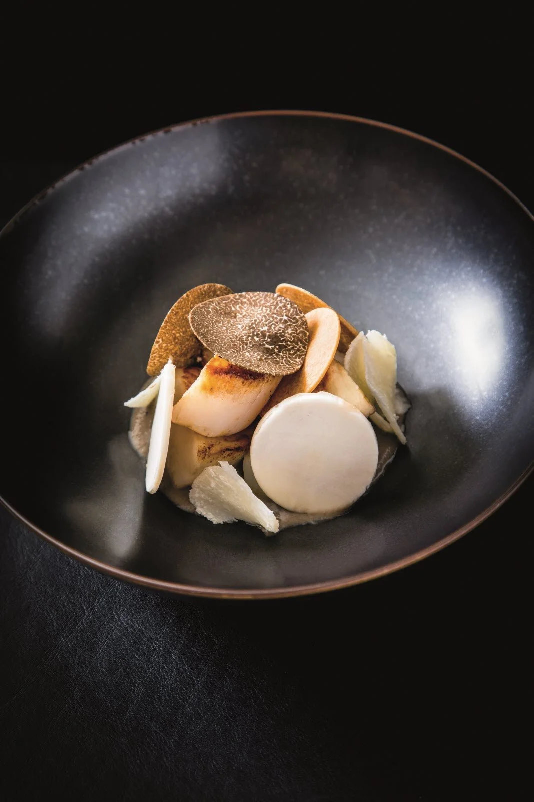 Assiette avec des tranches de champignon, des chips de truffe et des lamelles d'ail ou d'oignon.