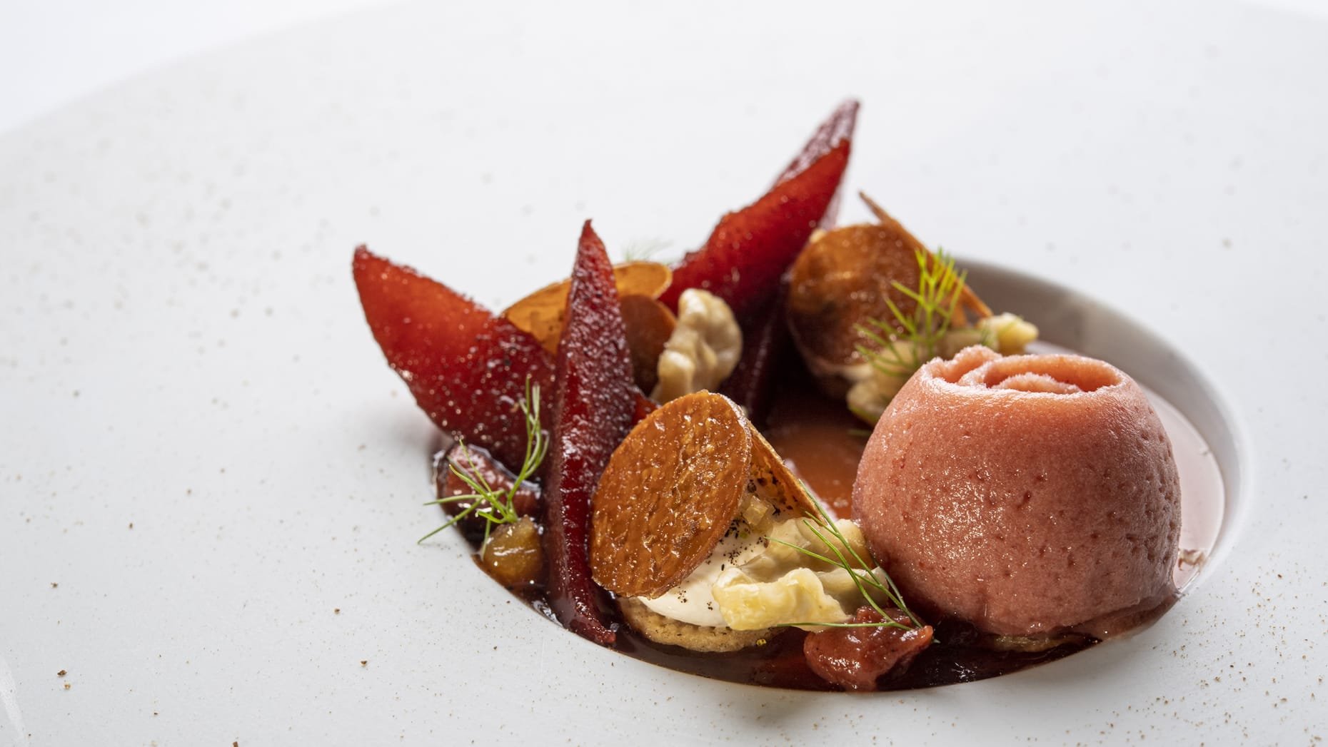 Assiette de dessert avec sorbet rose, fruits secs, et décoration fine