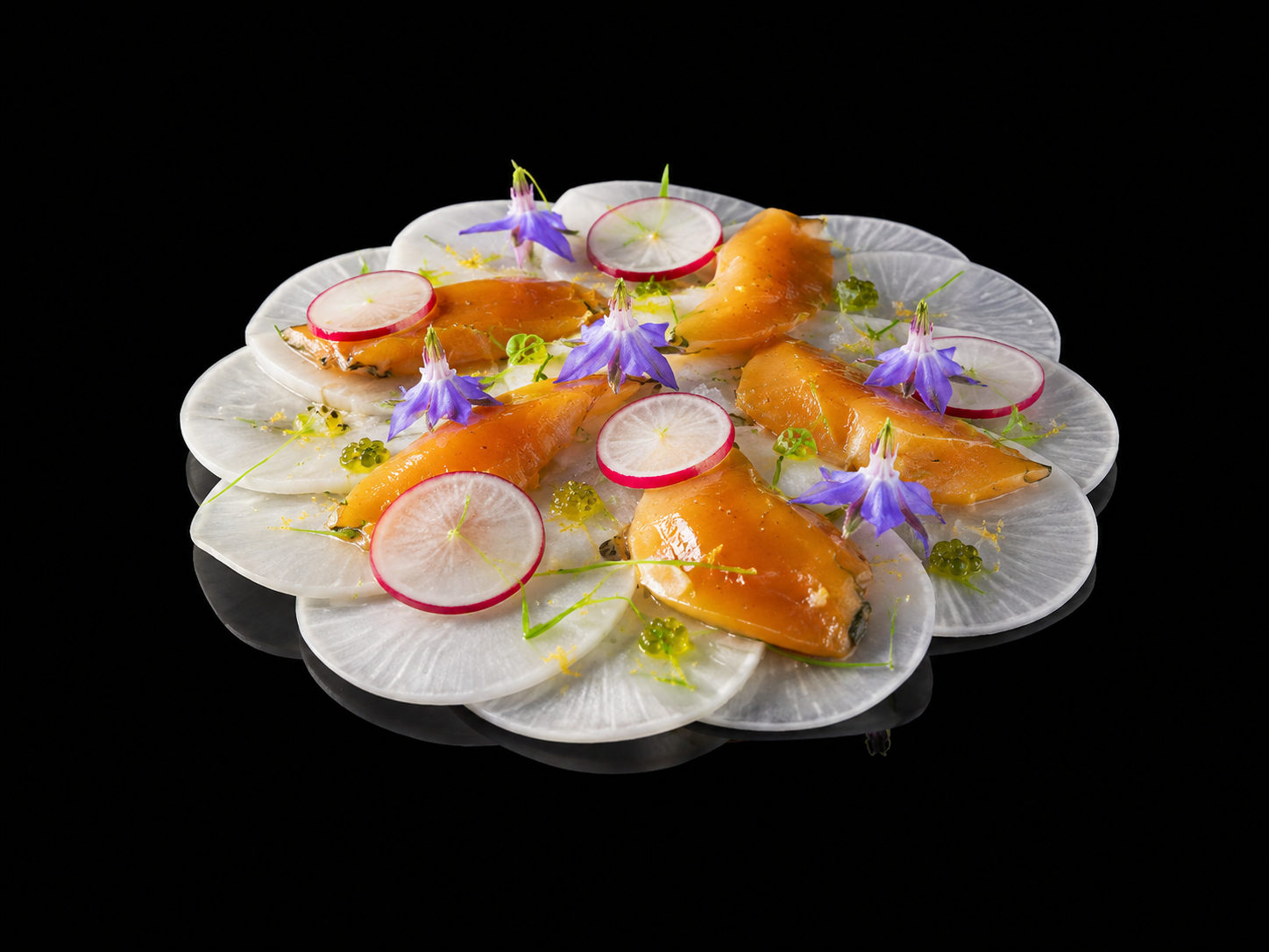 Un plat avec des tranches de radis blanc, des morceaux de poisson orange, garnis de fleurs violettes, de radis rouge, et de petites herbes vertes sur un fond noir.