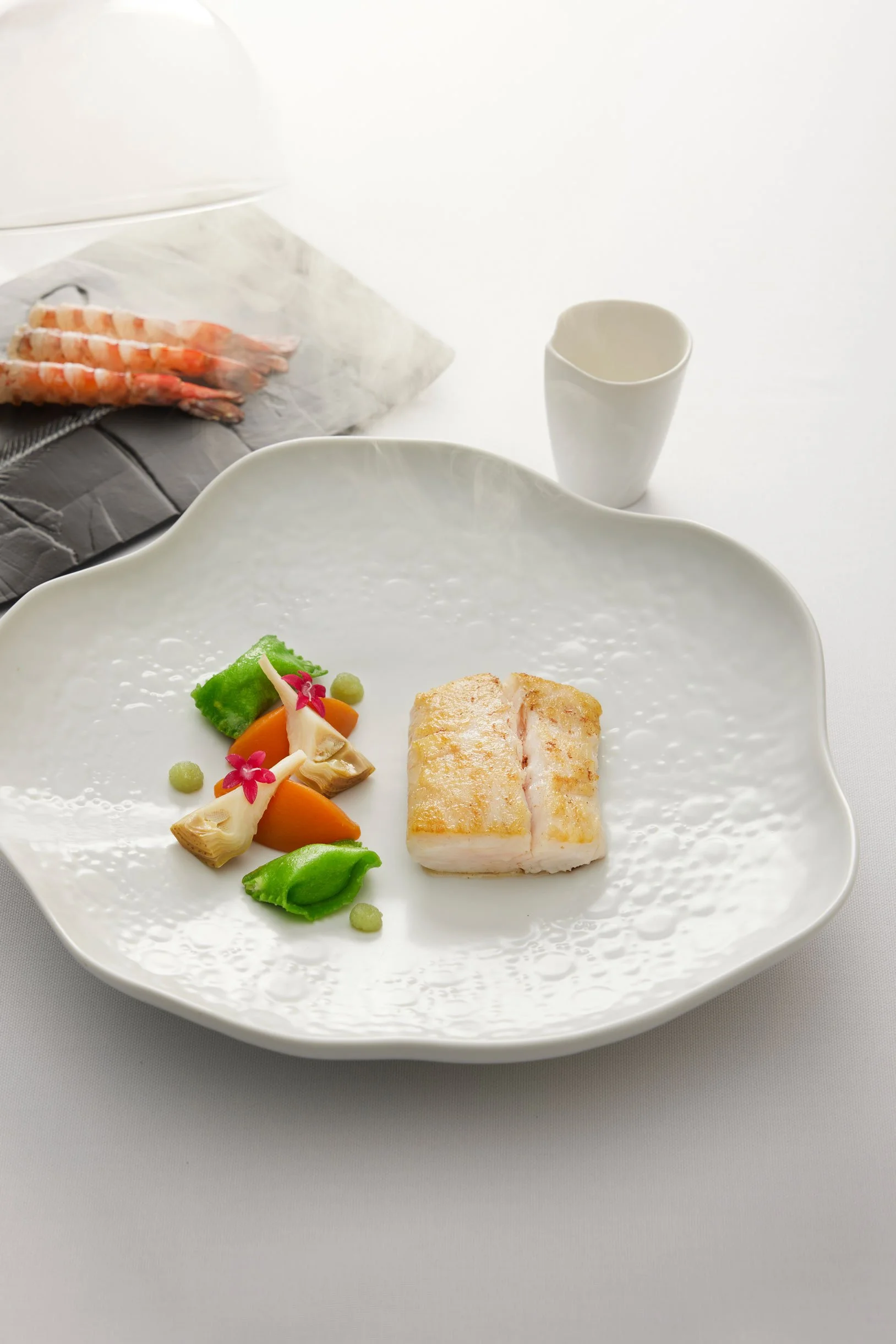 Passe de poisson avec légumes, fleurs comestibles et petites sphères vertes sur une assiette blanche