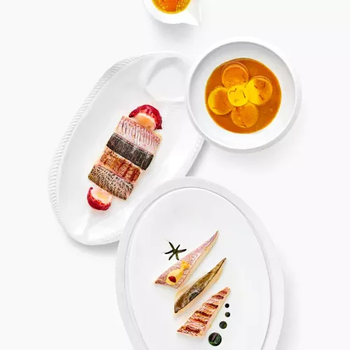 Assiette avec plusieurs morceaux de sushi, bol de soupe avec citron, et une petite tasse de thé ou boisson orange.