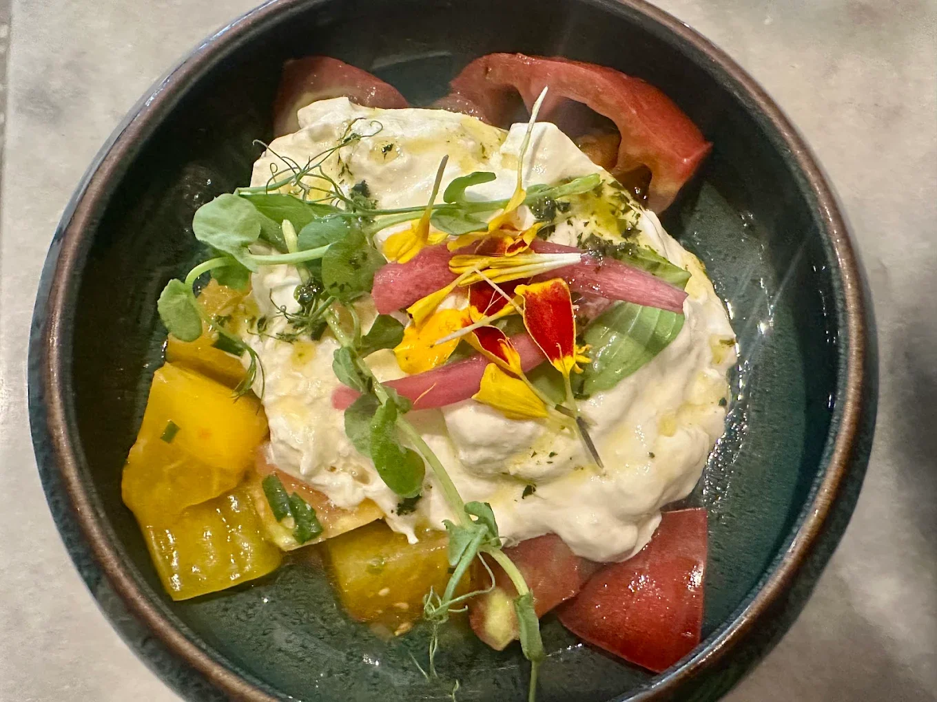 Une assiette de salade composée avec de la laitue, des morceaux de tomates, de la crème, des pousses vertes et des fleurs comestibles.