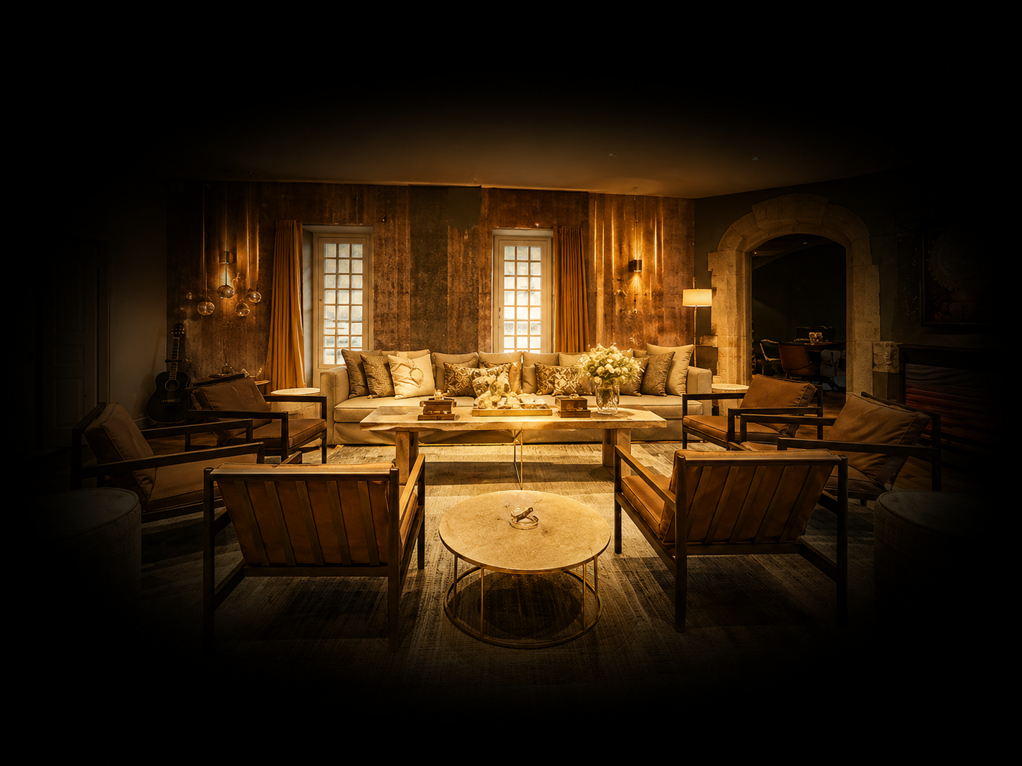 Salon intérieur chaleureux avec un grand canapé, quatre fauteuils en bois avec coussins, une table basse, une guitare, et un éclairage tamisé