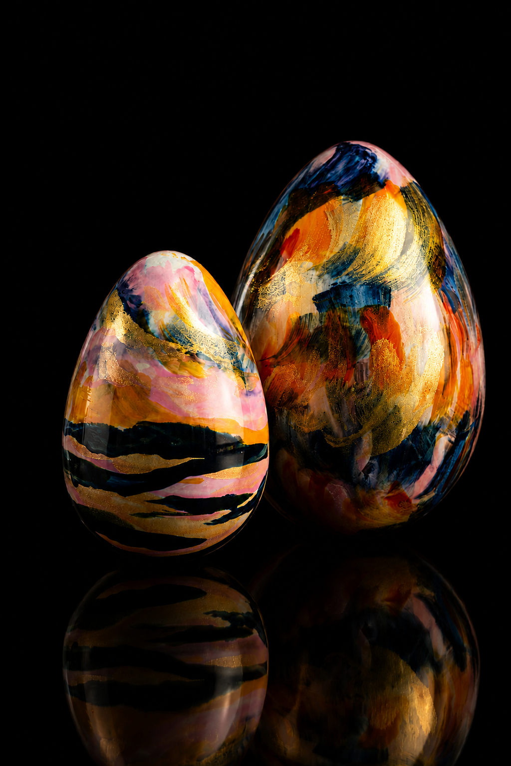 Deux œufs décoratifs peint à la main dans des couleurs vives, posés sur une surface noire avec leur reflet visible en dessous.