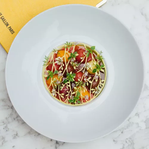 Assiette de carpaccio de boeuf garnie de micro-pousses et de fleurs comestibles, avec une vinaigrette légère.