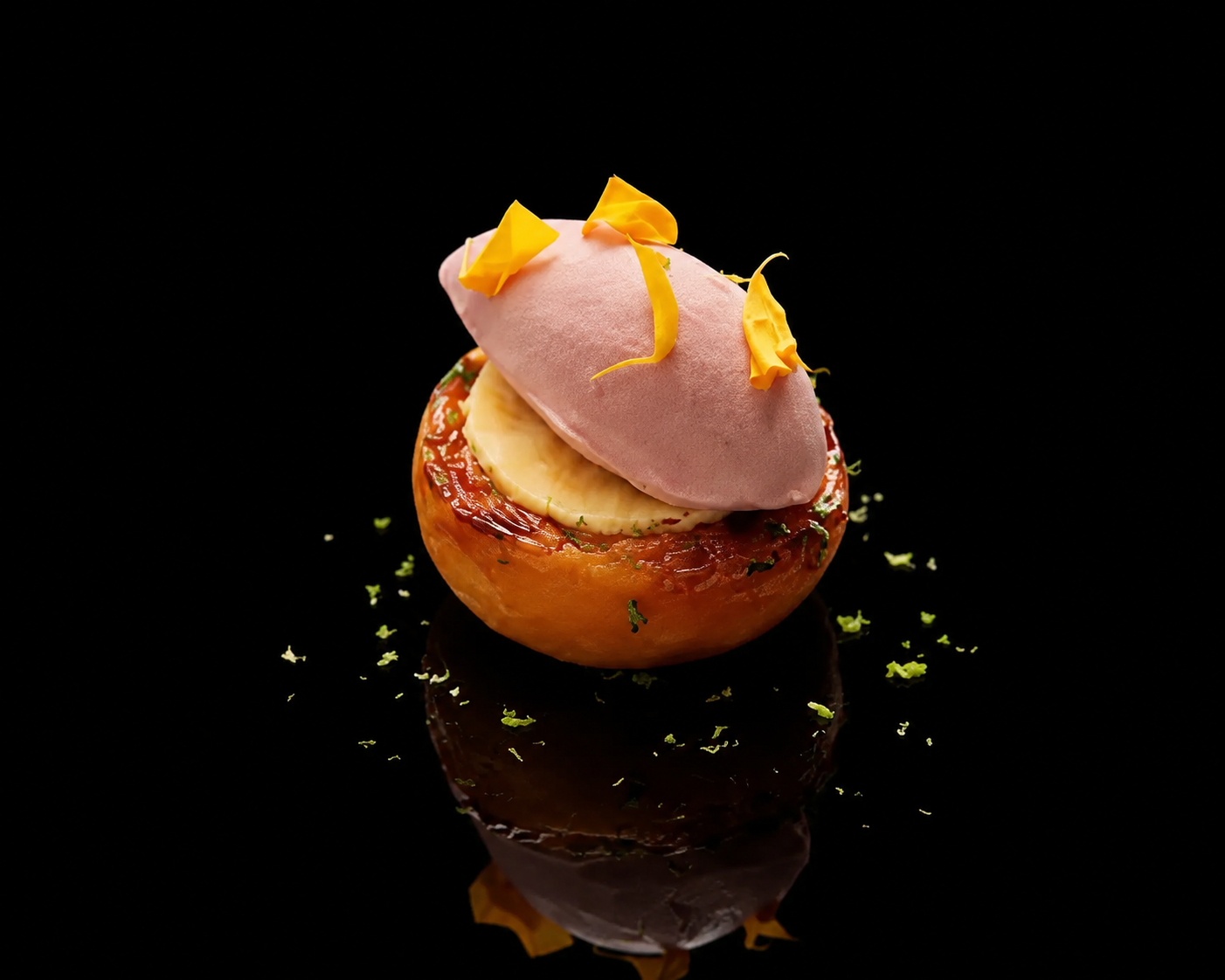 Une présentation culinaire sophistiquée avec une pomme évidée, garnie de banane, meringue rose, fleurs jaunes et herbes, sur un fond noir