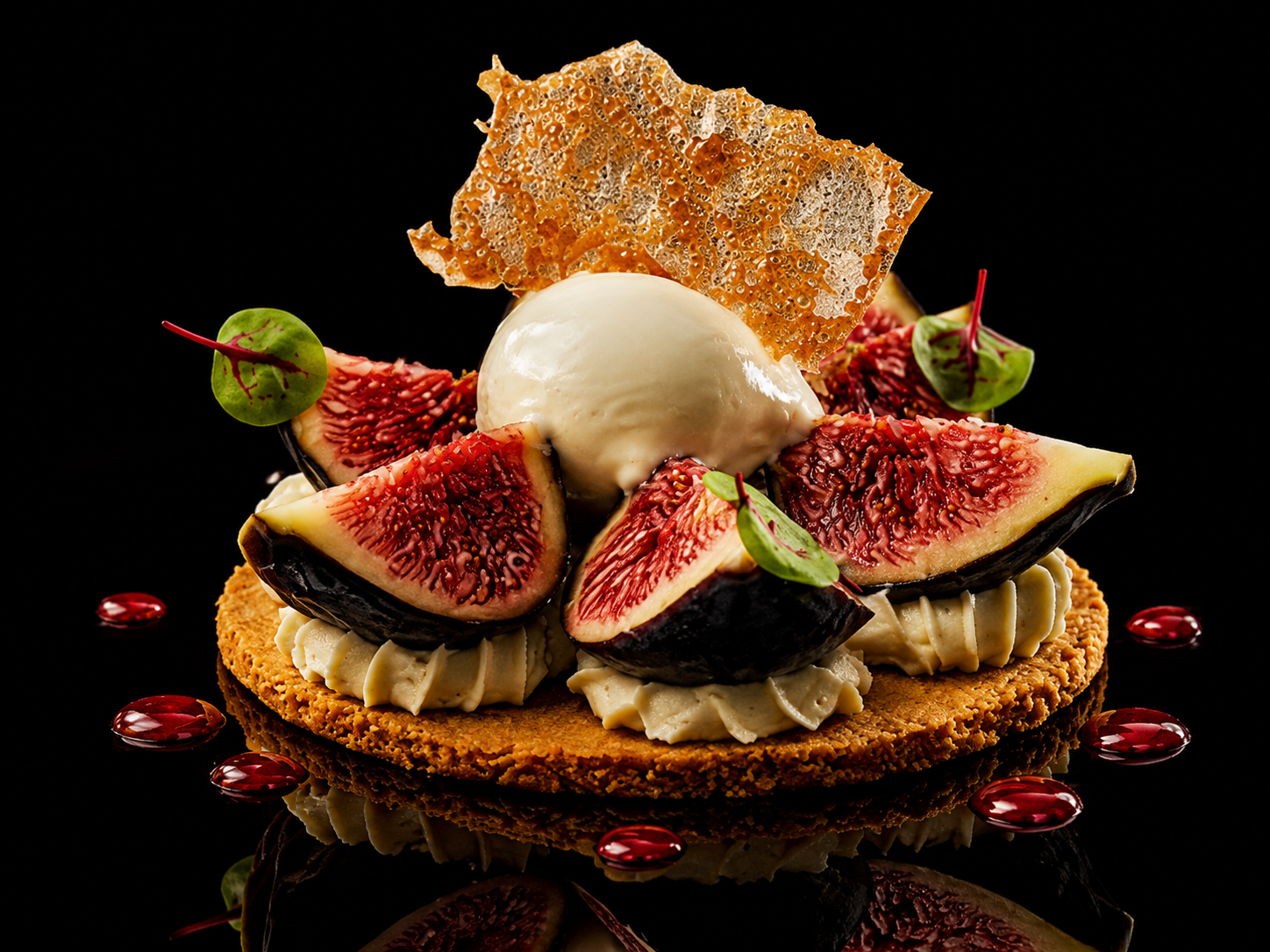 Gâteau élégant avec des figues fraîches, une boule de glace à la vanille, une feuille de caramel croustillant et des petites feuilles vertes décoratives, décoré de perles de gelée rouge et présenté sur un fond noir.