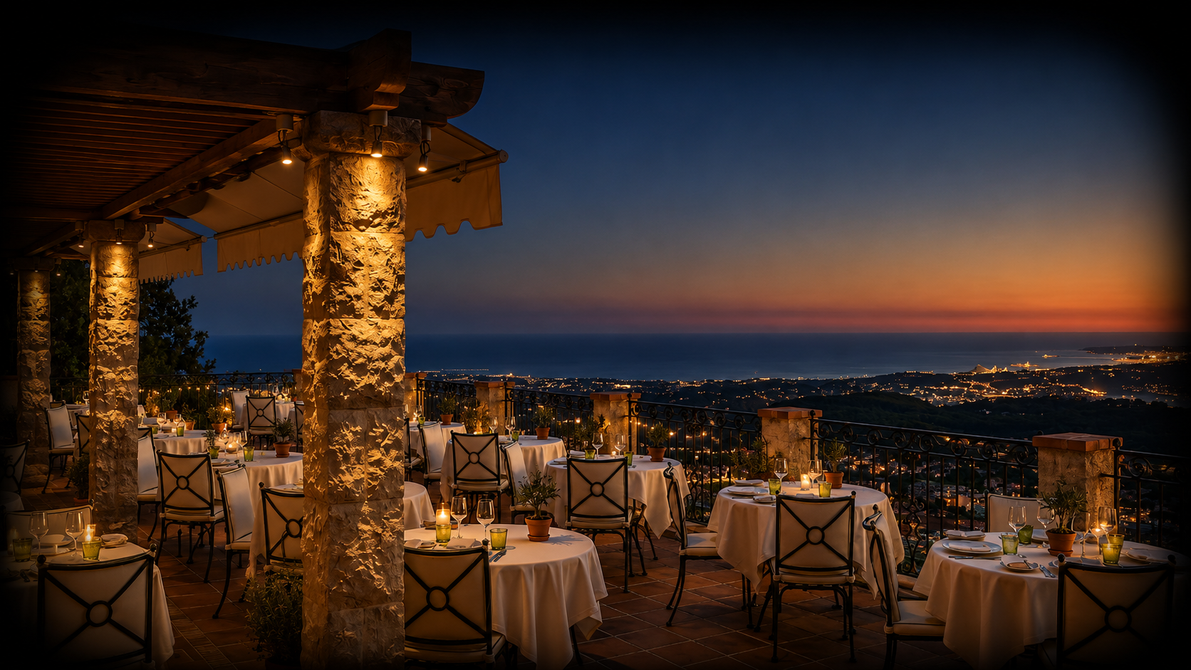 Terrasse de restaurant avec tables, chaises, bougies et vue sur la mer au crépuscule.