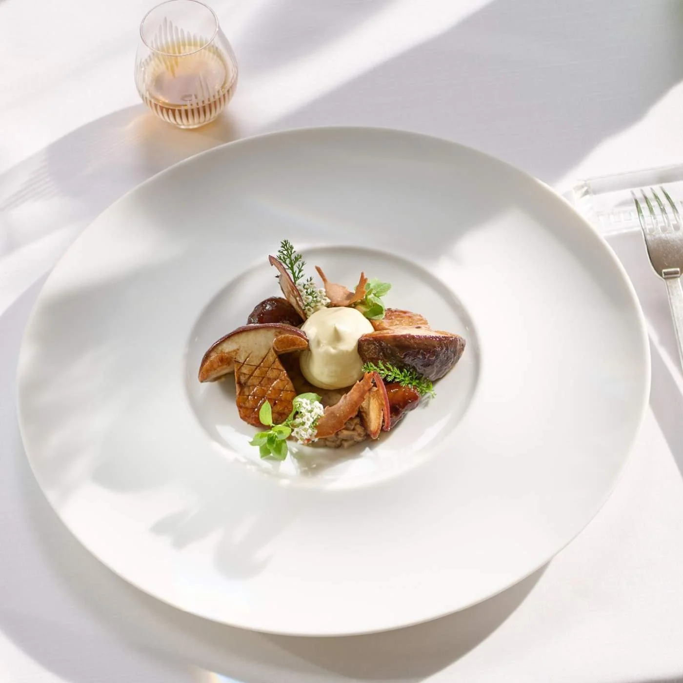 Assiette de viande avec légumes et sauce, accompagnée d'un verre de vin rosé, sur une table blanche.