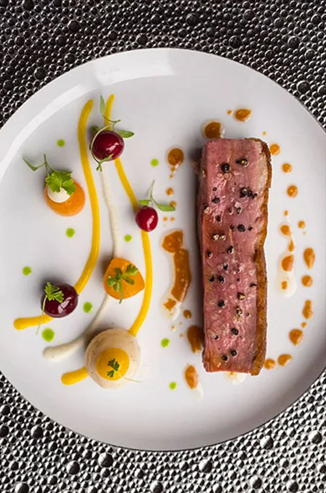 Assiette de filet de viande avec décoration colorée, cerises et sauces variées.