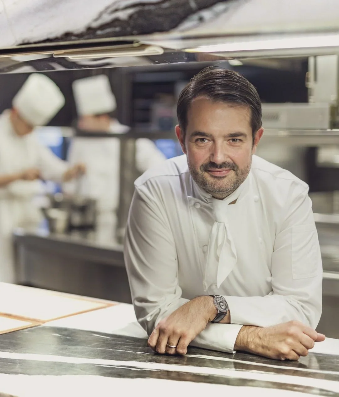Un dessert en forme de cylindre, appelé Bûche de Noël, avec un aspect blanc et une garniture dorée sur le dessus, présenté sur une assiette noire.