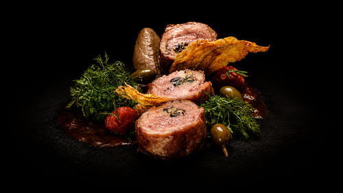 Assiette de viande farcie entourée de légumes et de garnitures, présentation gastronomique sur fond noir.
