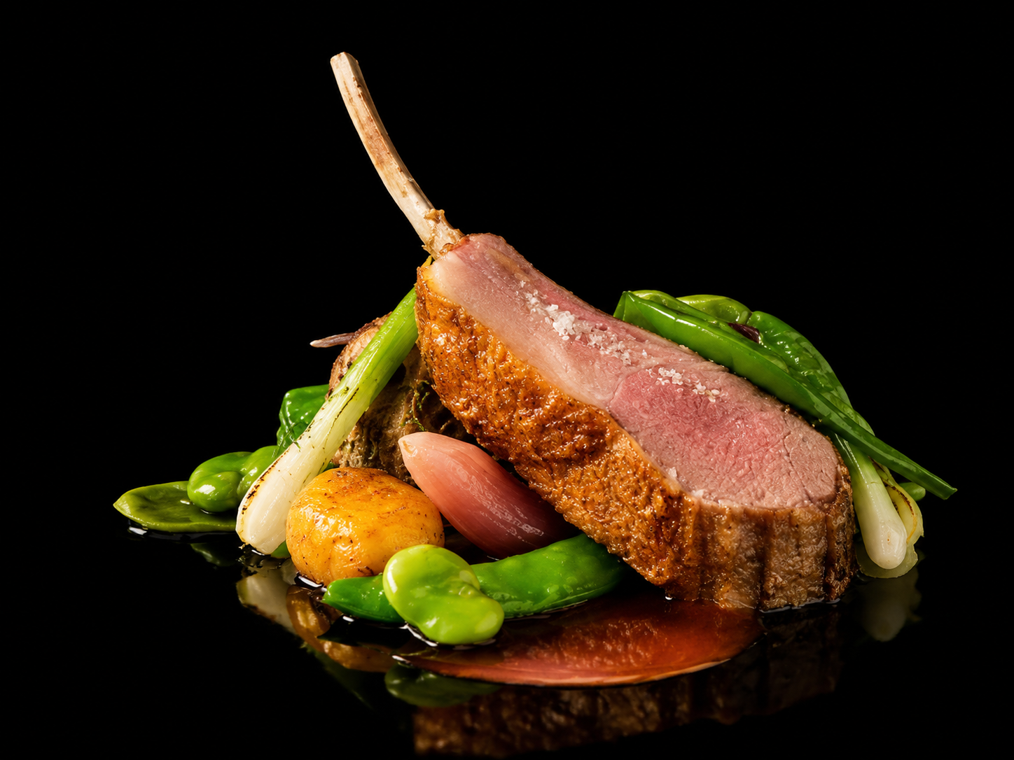 Une tranche de viande cuite, accompagnée de légumes verts et de petits légumes, sur une surface noire
