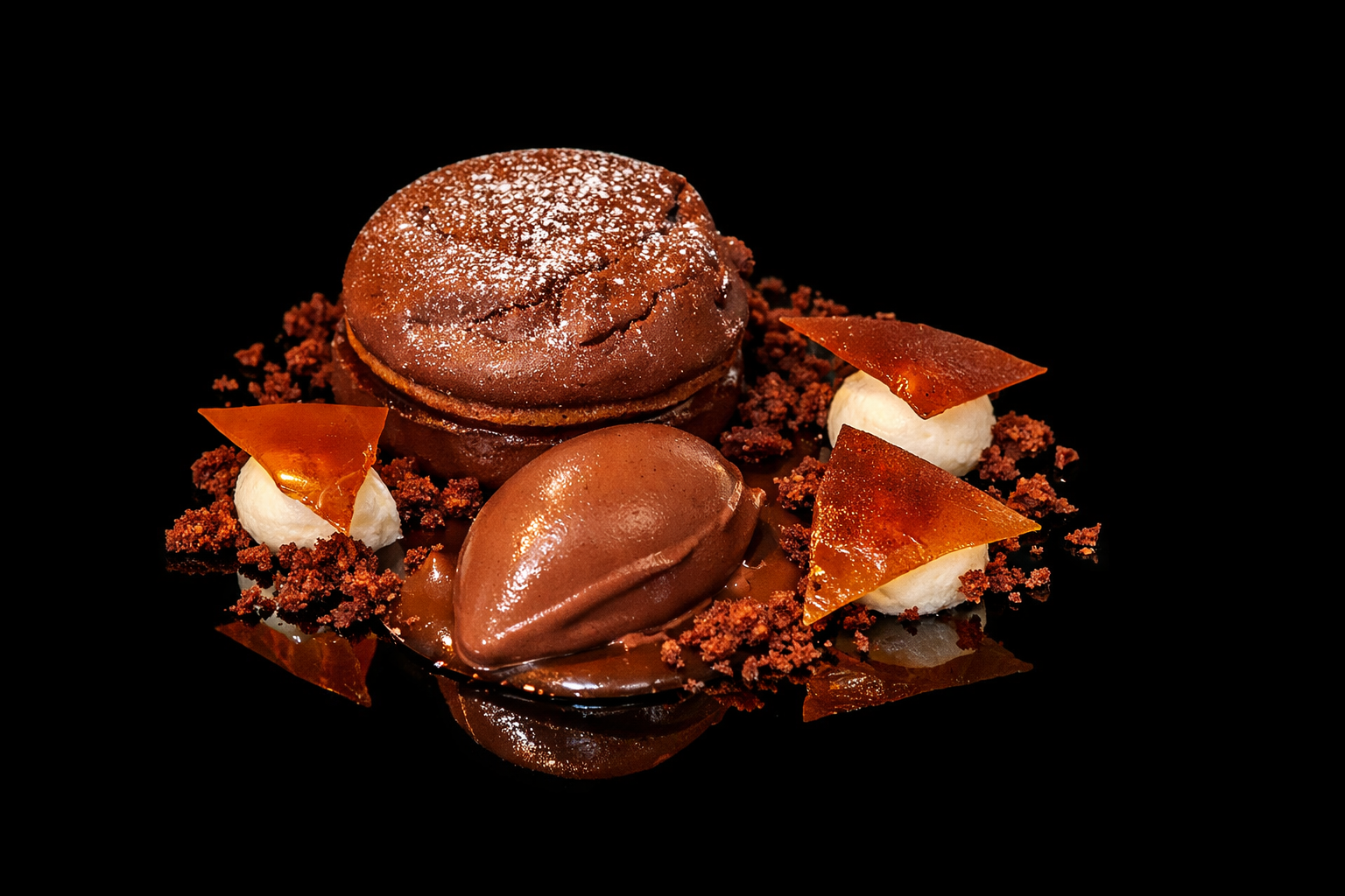 Un dessert chocolaté avec deux morceaux de glace, des morceaux de caramel, des éclats de biscuit et une poudre de cacao sur un fond noir.