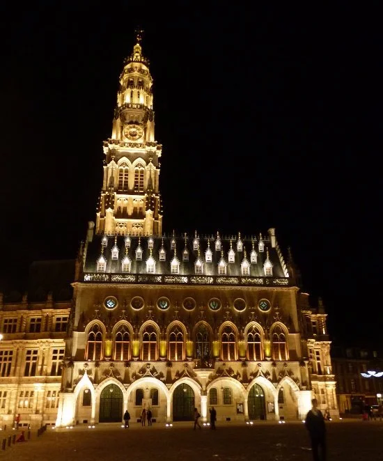 Un bâtiment historique illuminé la nuit, avec une grande tour centrale ornée de lumières